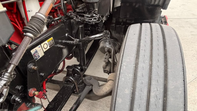 Kenworth T680 engine bay and front suspension showing exhaust manifold and large front tire from a used conventional sleeper truck.