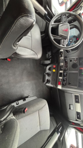 Kenworth T680 interior cabin view showing driver seat, steering wheel with Kenworth emblem, and dashboard with controls and cup holders.