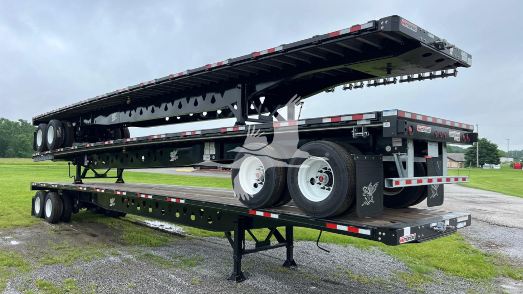 Manac steel flatbed trailer shown in extended position with dual rear axles and decking visible; black with reflective safety stripe and white wheels.