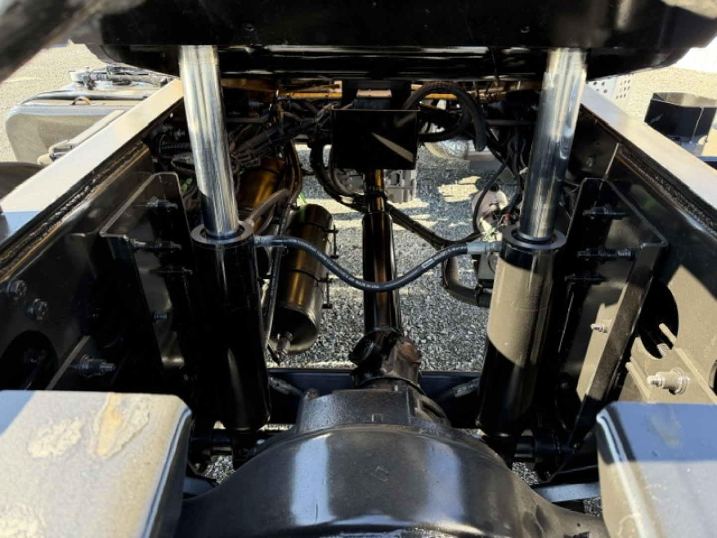 Trucks chassis view showing heavy-duty rear suspension with dual hydraulic cylinders, drive shaft, and wiring harness under the bed of a 2018 Capacity Sabre DOT truck.