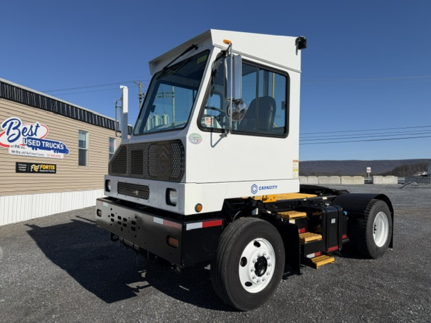 Truck cab and chassis showing Cummins logo on white cab with large front grille and side mirrors; yard background with Best Used Trucks sign; bare chassis with rear wheels.