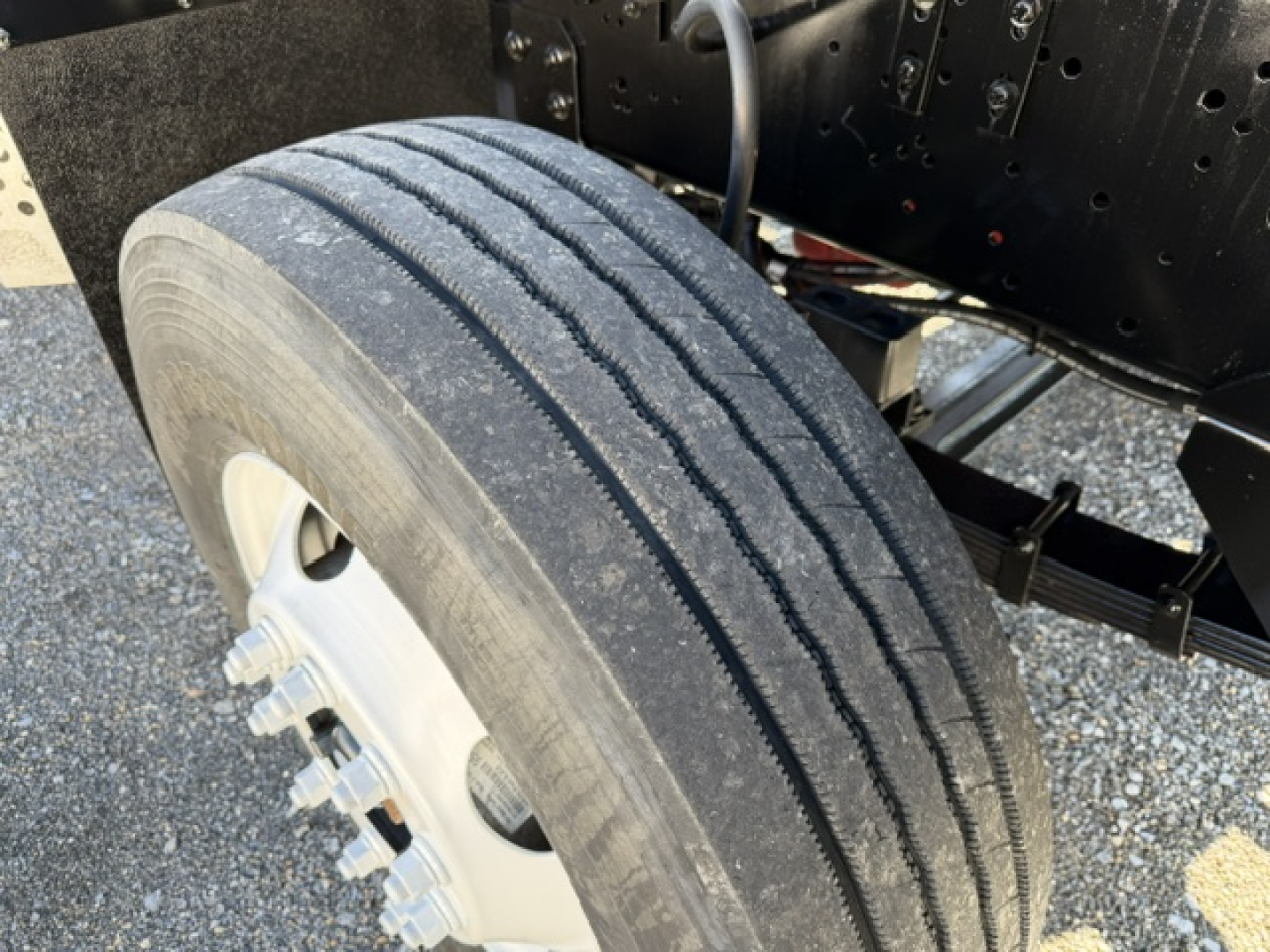 Tire and wheel assembly on a truck chassis with dual rear wheels visible, showing tread wear and metal lug nuts.