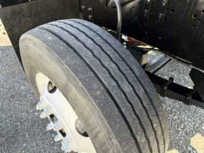 Tire and wheel assembly on a truck chassis with dual rear wheels visible, showing tread wear and metal lug nuts.