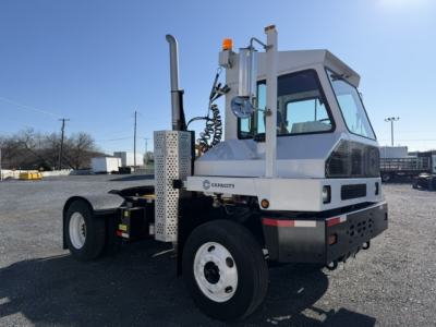 Capacity Sabre yard truck tractor showing white cab with stacked exhaust, orange beacon, and spare wheel; side view with Capcity branding on panel.