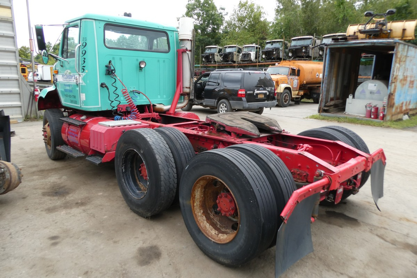 Truck chassis of a 1997 International 8100 Daycab showing rear wheels and chassis frame in red with turquoise cab, used condition.