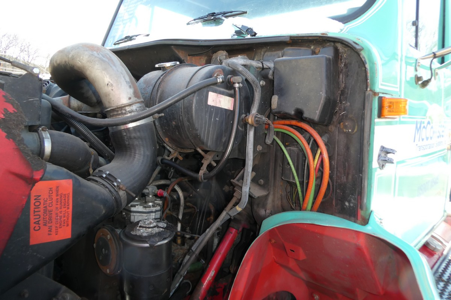 Truck engine bay of a 1997 International 8100 daycab showing intake manifold, air intake hose, wiring harness, coolant reservoir, and alternator.