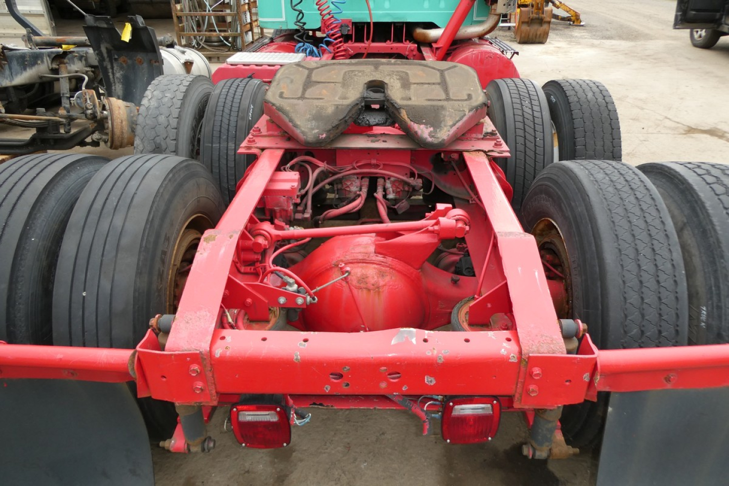 Rear view of a red International 8100 truck chassis showing dual rear axles and fifth wheel, with visible suspension and drive components.