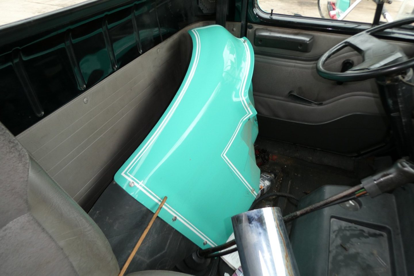 Interi or cab of a 1997 International 8100 with turquoise front fender panel inside cabin showing steering wheel and dash.