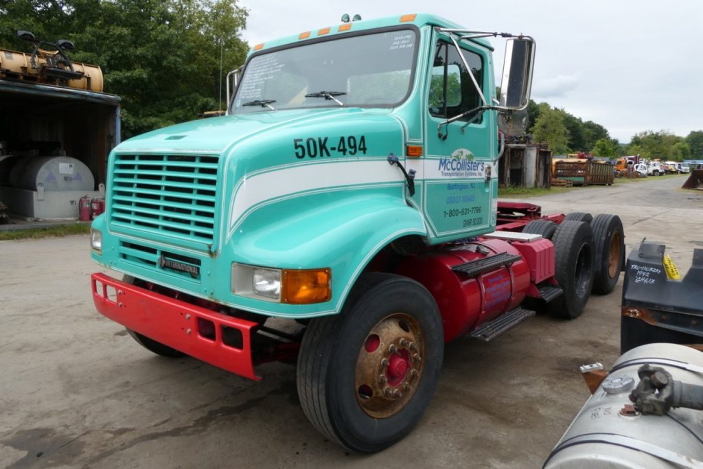International 8100 daycab truck showing teal cab with 50K-494 on door and red chassis in an outdoor lot.
