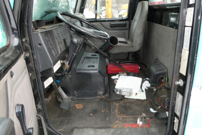 Interior of a 1997 International 8100 cab showing steering wheel, dashboard, worn floor mat, and scattered papers near the seat.