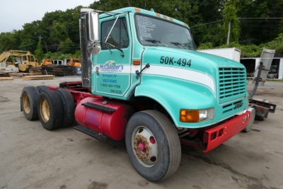 International 8100 truck cab in teal with white stripes and red bumper showing 50K-494 on side and McCollister's logo on door; tanker mounting behind, visible cabinets and wheels.