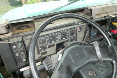 Dashboard and steering wheel of a cab showing multiple gauges and switch cluster; worn dash with rectangular instrument panel.
