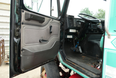 Truck cab interior visible with open door showing steering column, dashboard, pedals, and door panel on an International 8100 cab.