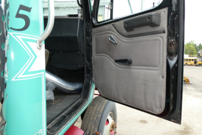 Truck cab interior door area of a 1997 International 8100 sighted with open door showing grey door panel and part of green cab with star logo.