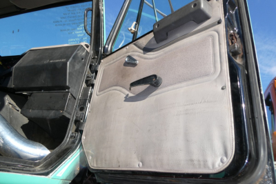 Truck cab interior door panel with manual window crank in a 1997 International 8100 conventional daycab showing beige door panel and black floor area