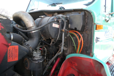 Truck engine bay of a 1997 International 8100 daycab showing intake manifold, air intake hose, wiring harness, coolant reservoir, and alternator.