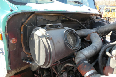 Engine bay of 1997 International 8100 with exposed air intake and cooling hoses; visible hoses, clamps, and cylindrical component; details of engine bay machinery.