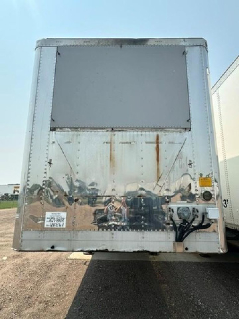 Rear view of a 2006 utility refrigerated trailer showing a reflective stainless panel with rust stains and a small white sticker at lower left and hitch components on the right.