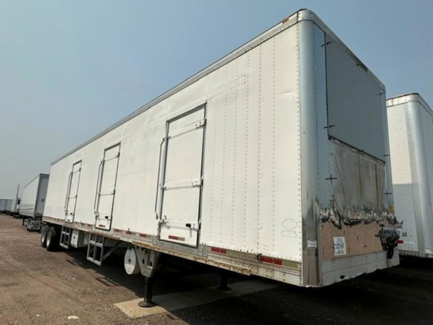 Utility reefer trailer with side doors and rear doors, white exterior, utility trailer in a lot.