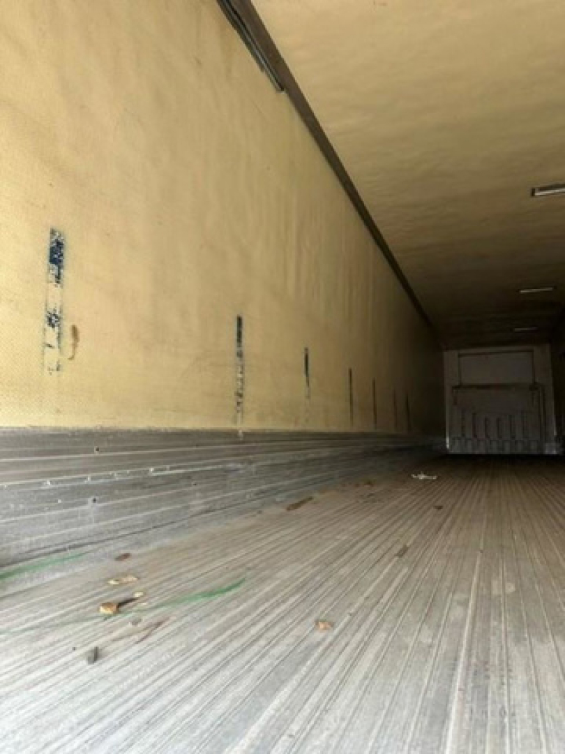 Trailer interior cargo area of a refrigerated utility trailer, long empty box with ribbed floor and side walls, some debris on the floor.