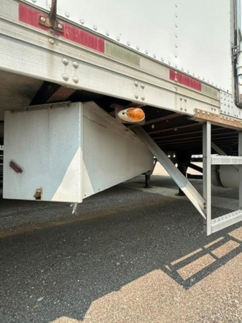 Trailer undercarriage showing a white diamond plate storage box and amber side marker light under a refrigerated trailer.