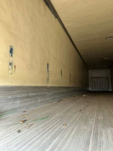 Trailer interior cargo area of a refrigerated utility trailer, long empty box with ribbed floor and side walls, some debris on the floor.
