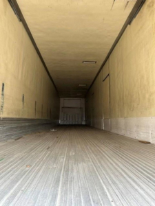 Trailer interior showing empty refrigerated cargo space with ribbed floor and light at ceiling.