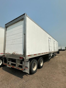 Refrigerated utility trailer showing white box with rear and side doors, triple axle tires, and reflective striping.