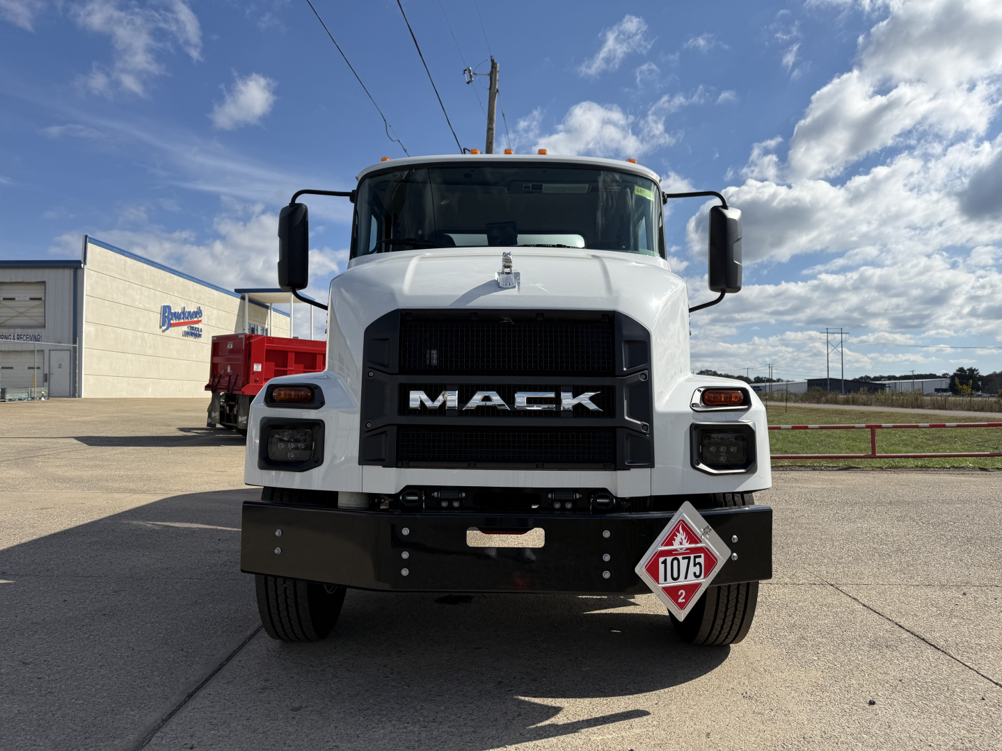 Mack MD7 truck front view showing large black grille with MACK letters, white cab, bumper, and hazard placard 1075 on lower right front.