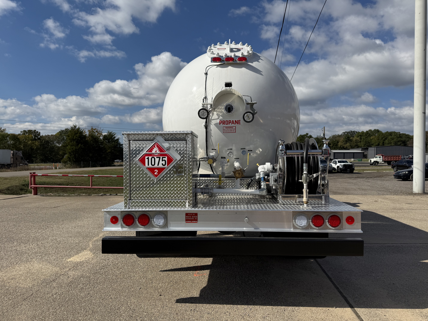Back view of a new 2026 Mack MD7 tanker truck with a large round tank, safety placards, hoses, and rear equipment platform.