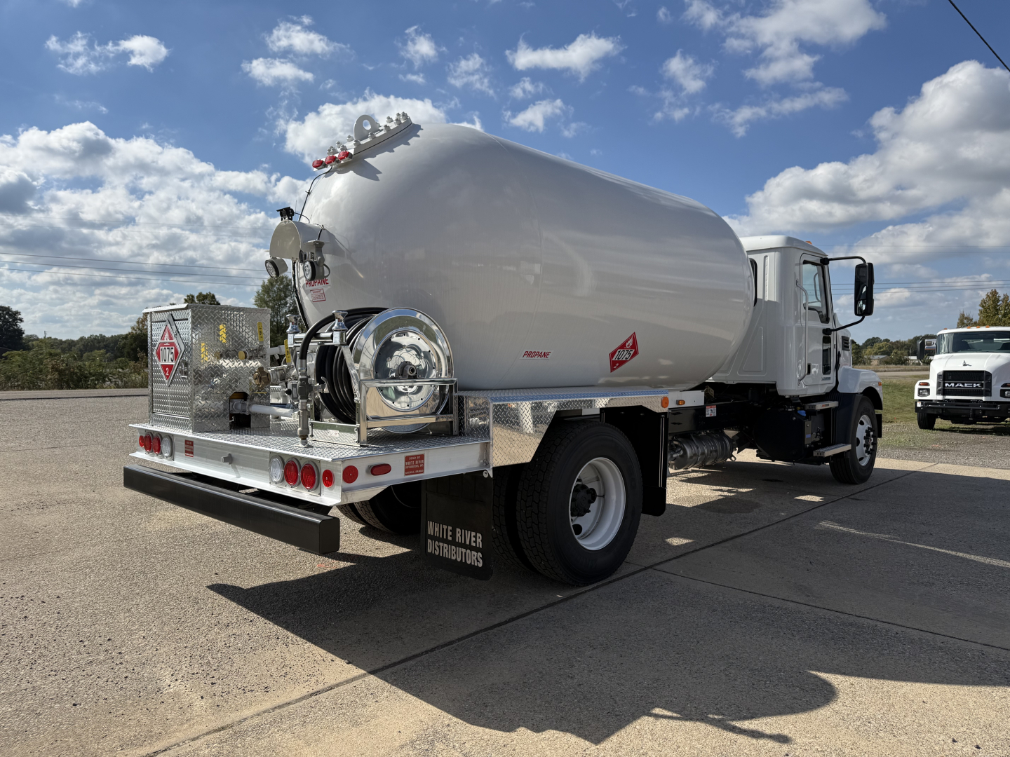Tank truck rear/side view showing cylindrical fuel or water tank on chassis with rear platform, taillights, and associated equipment.
