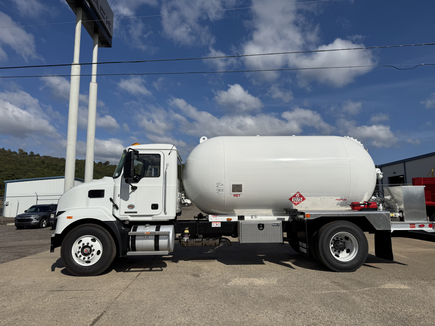 Large white Mack MD7 tanker truck side view showing cylindrical tank and cab. Visible text includes hazard placard and label on tank along with chassis components.