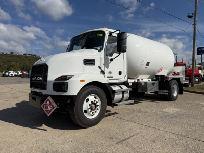 New 2026 Mack MD7 front-left view showing cylindrical tanker body and safety placards on white truck.