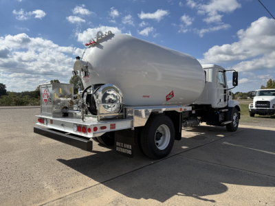 Tank truck rear/side view showing cylindrical fuel or water tank on chassis with rear platform, taillights, and associated equipment.