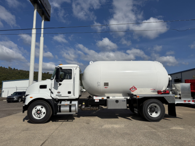 Large white Mack MD7 tanker truck side view showing cylindrical tank and cab. Visible text includes hazard placard and label on tank along with chassis components.
