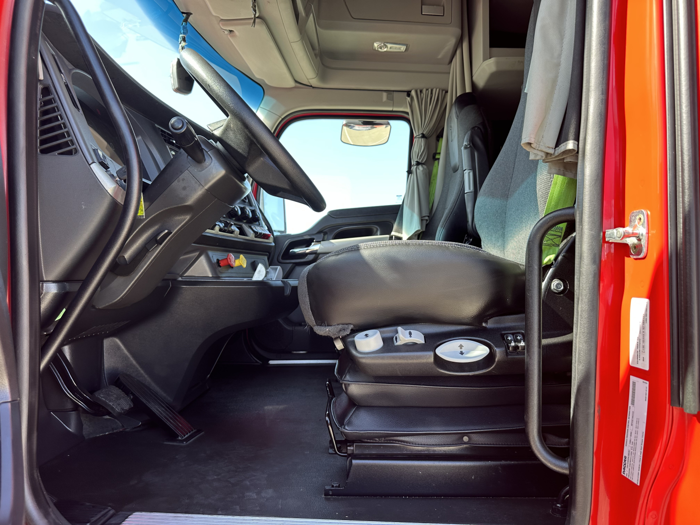 Kenworth T680 truck cab interior view showing steering wheel, driver's seat, dashboard, and entry door.