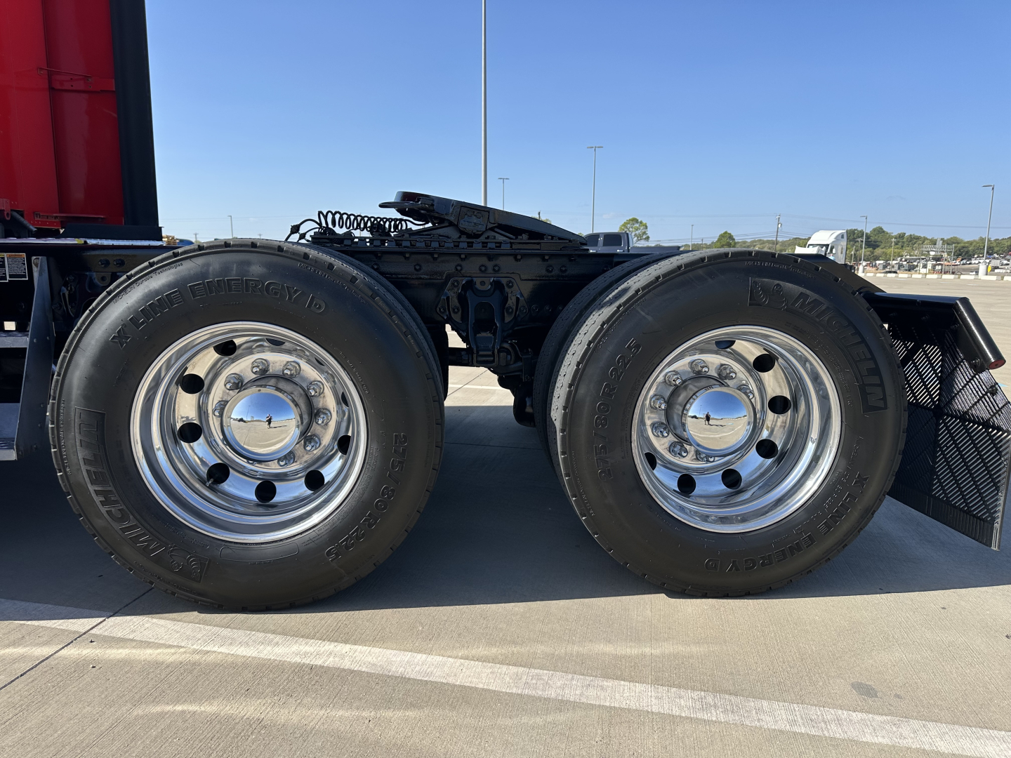 Dual rear wheels on a Kenworth truck with chrome hubs and black tires; part of the chassis and undercarriage visible.