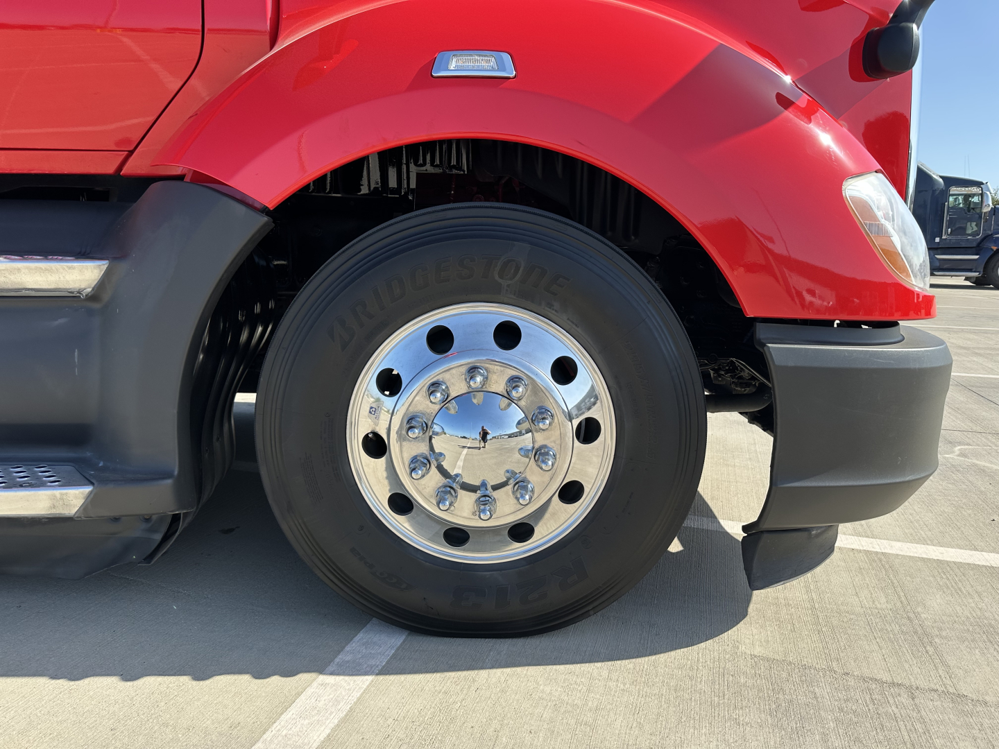 Kenworth T680 front wheel area showing Bridgestone tire and chrome wheel hub with red truck fender and black bumper.