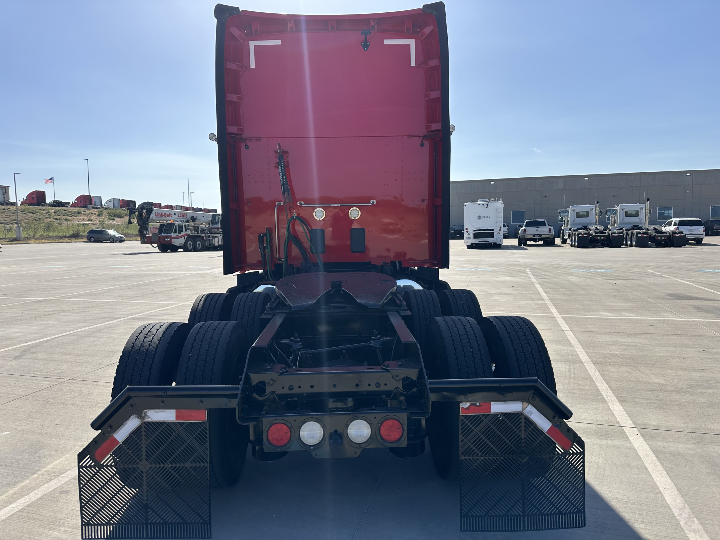 Rear view of a red Kenworth T680 semi-truck tractor showing chassis, dual rear axles, and fifth-wheel with mud flaps.