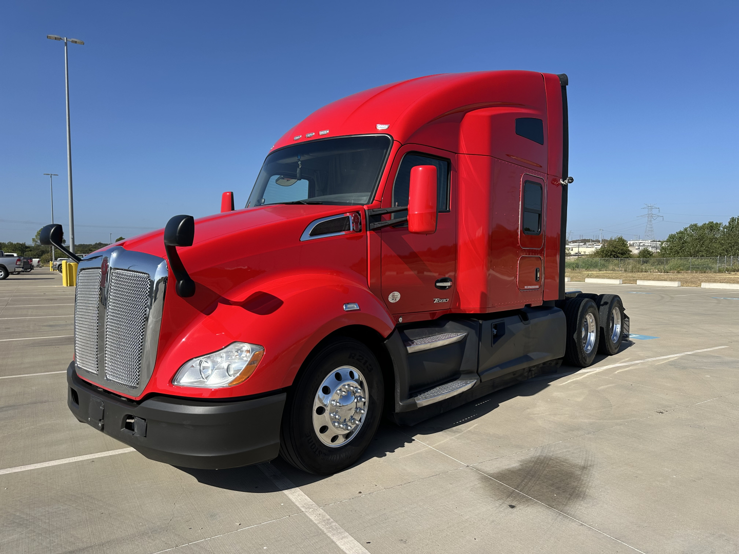 Kenworth T680 sleeper cab tractor in red, side view, showing front grille, headlights, mirrors, and dual rear axles with chrome wheels.