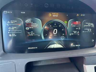 Dashboard display inside a Kenworth truck showing digital gauges and warning icons. Visible text includes Fuel Low Add Fuel, 0 MPH, Trip 158.6 MI, 303,630.6 MI, 96°F, 135°C, various oil temp and pressure indicators, and battery/air/DEF ic