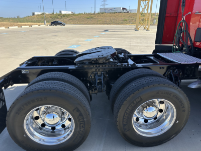 Kenworth truck chassis side view showing dual rear axles and chrome wheels with fuel tank and engine components visible underneath the cab.
