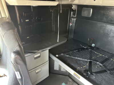 Kenworth T680 sleeper cab interior showing bed area, storage drawers, and overhead compartments with cables.
