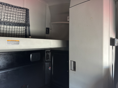 Kenworth T680 sleeper cab interior showing cargo area and partition with storage cabinet and netted shelf.