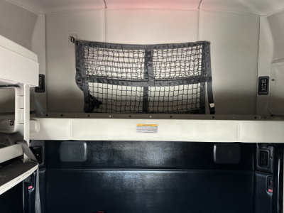 Kenworth sleeper cab interior showing a cargo net and storage shelf, with a white cabinet on left and metal framework.