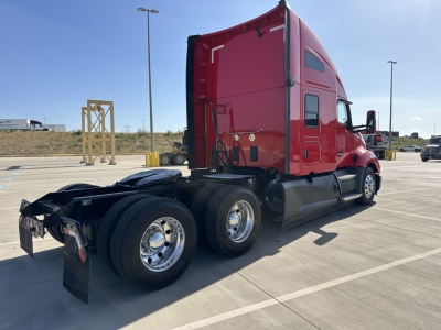 Kenworth T680 tractor in red, left rear view showing three axles, dual rear wheels, fuel tanks, and sleeper cab.