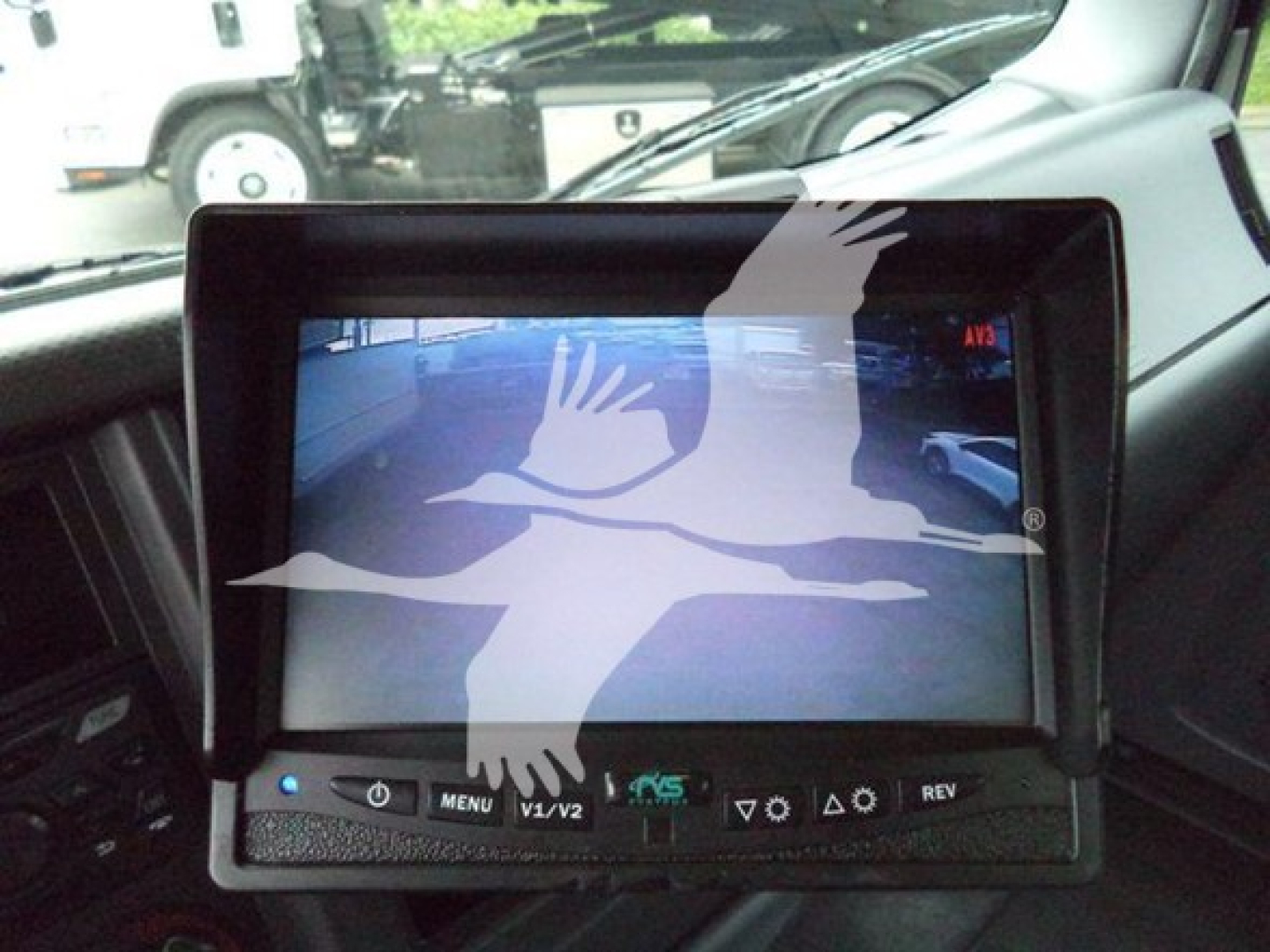 In-cab display screen mounted on dash with control buttons visible. Screen shows bird watermark overlay from image.