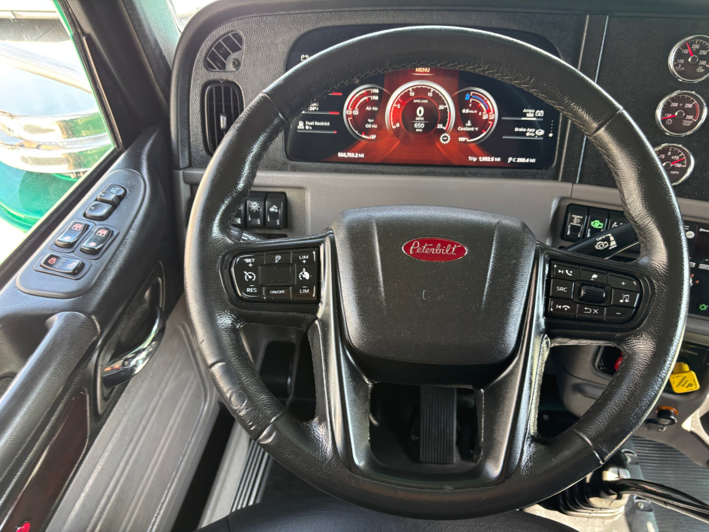 Peterbilt 389 truck cockpit with steering wheel and digital instrument cluster, dashboard controls, and tachometer readout visible