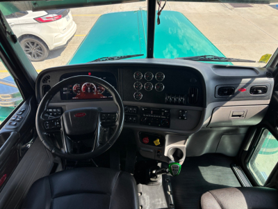 Peterbilt 389 cab interior view from driver seat showing dashboard gauges, steering wheel, shifter, and center console.