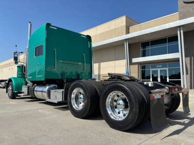 Peterbilt 389 conventional sleeper truck in teal green color, viewed from rear-left, showing tandem axle wheels and chassis hitch.